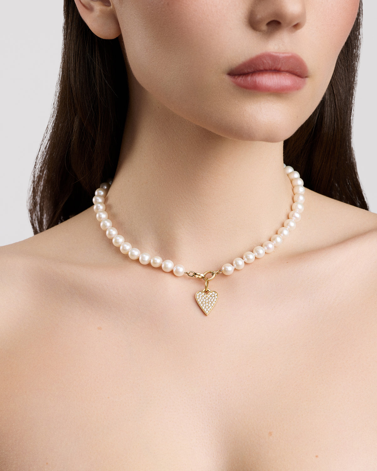 Pearl necklace with a heart-shaped charm worn by a model on a plain background