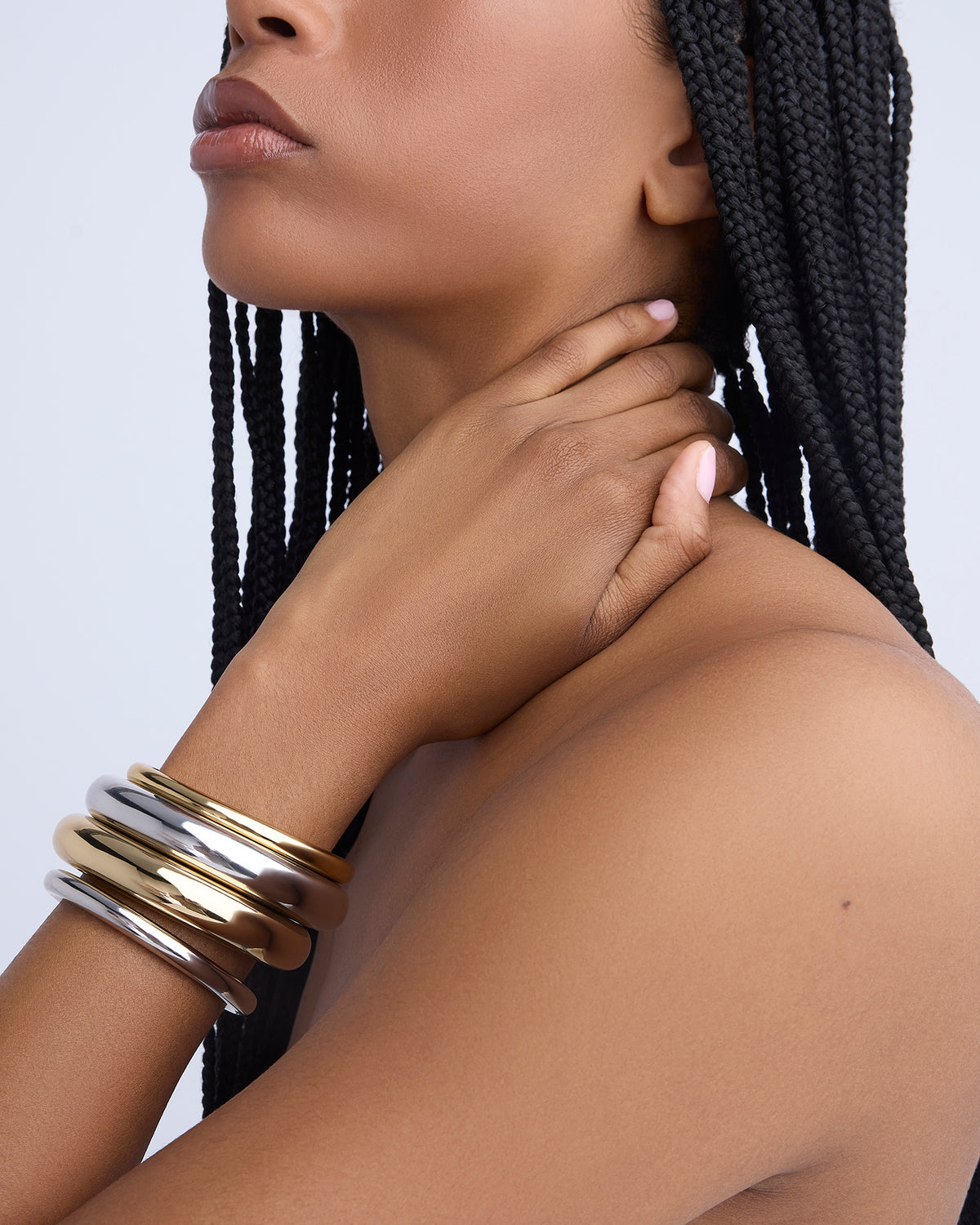 Woman wearing gold and silver bracelets on a plain background